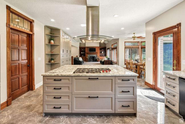 Kitchen featuring stainless steel gas stovetop, ceiling fan, island range hood, marble tiled floors, and gray cabinetry | Image 5