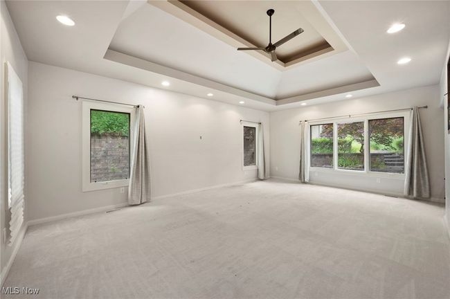 Carpeted first floor primary suite featuring a tray ceiling, plenty of natural light, recessed lighting, and a ceiling fan | Image 9