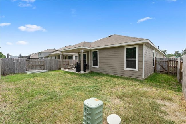 This photo shows a modest backyard featuring a covered patio attached to a single-story home with beige siding. The yard is enclosed by a wooden fence, providing privacy, and has a grassy area suitable for outdoor activities. | Image 19