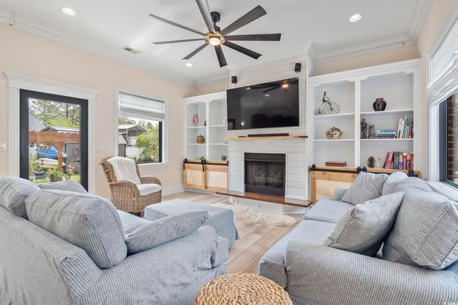 Living area featuring light wood finished floors, a ceiling fan, ornamental molding, a fireplace with raised hearth, and recessed lighting | Image 13