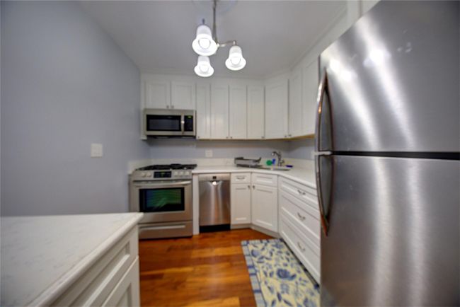 Kitchen featuring dark wood-type flooring, decorative light fixtures, stainless steel appliances, light countertops, and white cabinetry | Image 6