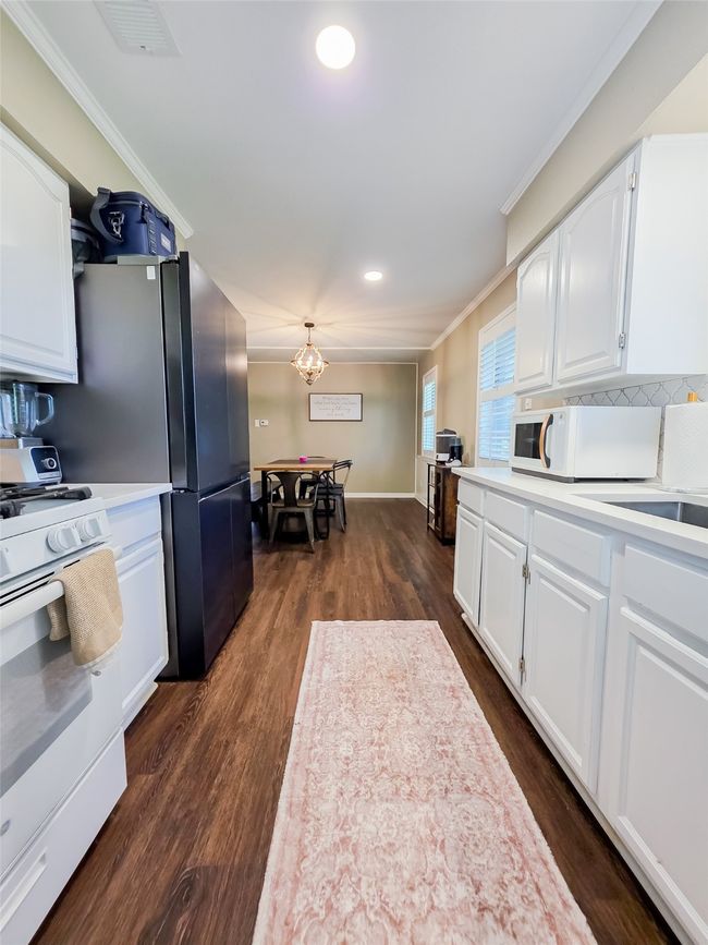 Kitchen featuring white appliances, ornamental molding, light countertops, white cabinets, and dark wood finished floors | Image 25