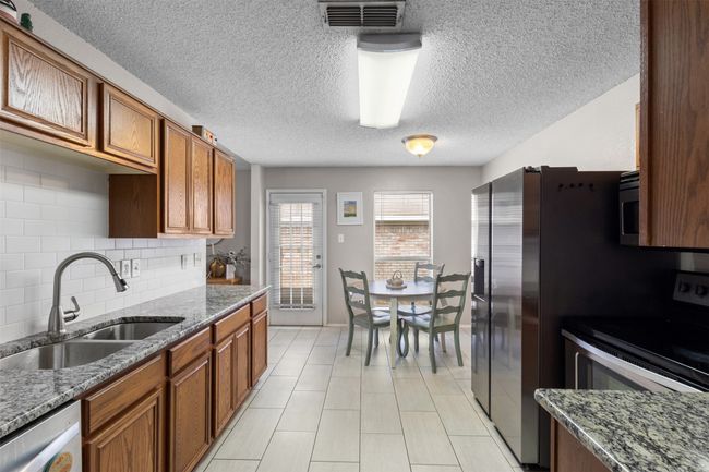 Kitchen featuring a sink, stainless steel appliances, a textured ceiling, decorative backsplash, and brown cabinetry | Image 13