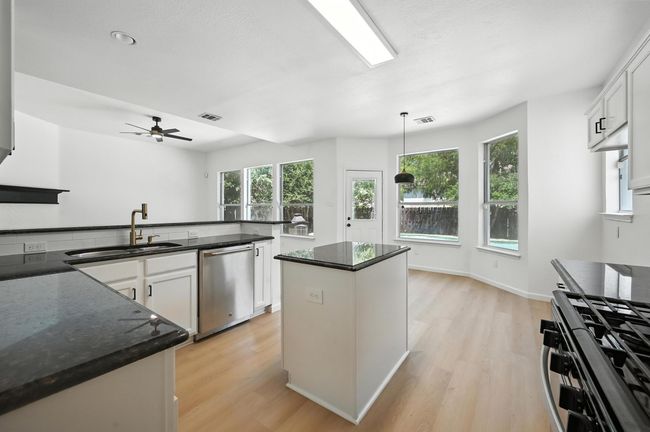 Kitchen featuring light wood finished floors, white cabinets, appliances with stainless steel finishes, a ceiling fan, and dark stone countertops | Image 6