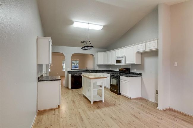 Kitchen featuring black appliances, arched walkways, light wood-style floors, white cabinets, and a sink | Image 13