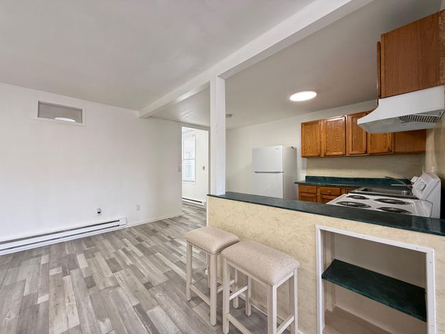Kitchen featuring white appliances, under cabinet range hood, visible vents, brown cabinetry, and light wood finished floors | Image 8