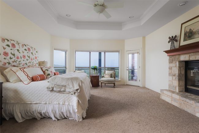 Carpeted bedroom featuring a stone fireplace, a tray ceiling, ornamental molding, access to outside, and a ceiling fan | Image 28