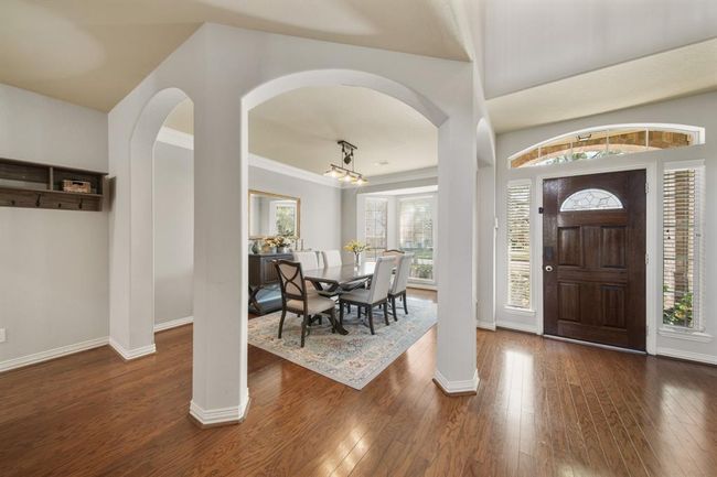 Surrounded by arched openings, the formal dining room with crown moulding & hanging light fixture includes hardwood floors. | Image 5