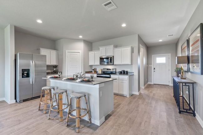 Kitchen with appliances with stainless steel finishes, a center island with sink, white cabinetry, tile flooring, and a breakfast bar | Image 10