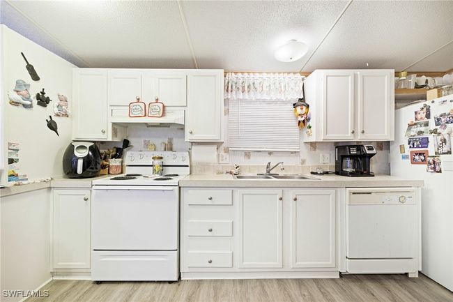 Kitchen featuring white appliances, a sink, LVT flooring, white cabinets, and a textured ceiling | Image 6