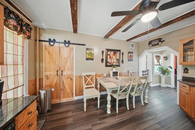 Dining room with beam ceiling, dark wood finished floors, a barn door, ceiling fan, and a wainscoted wall | Image 12