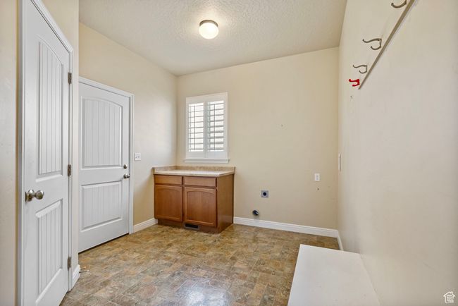 Laundry room featuring baseboards, a textured ceiling, cabinet space, stone finish flooring, and electric dryer hookup | Image 22