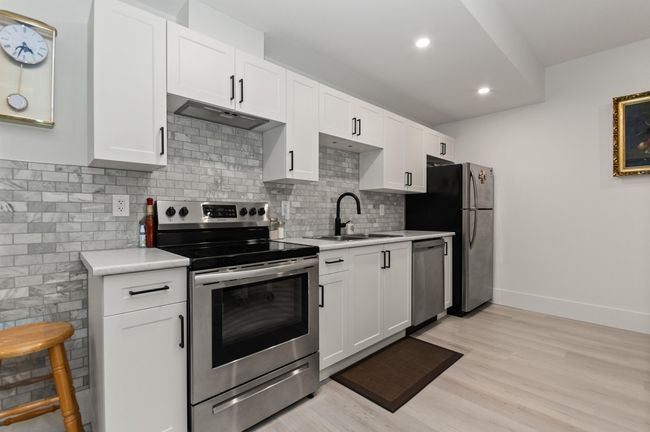 Kitchen featuring appliances with stainless steel finishes, a sink, light countertops, light wood-style flooring, and tasteful backsplash | Image 27