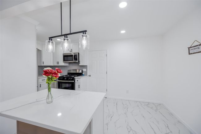 Kitchen with decorative backsplash, white cabinets, pendant lighting, black range with gas stovetop, and light stone counters | Image 15