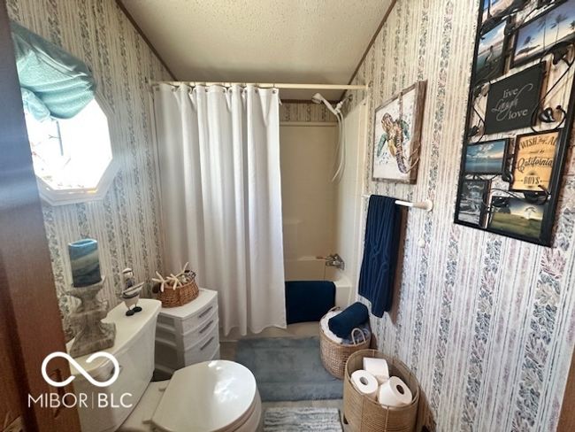 full bathroom with wallpapered walls, shower / tub combo with curtain, a textured ceiling, and toilet | Image 13