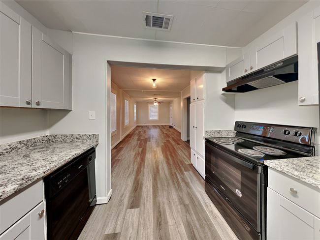 Kitchen featuring black appliances, under cabinet range hood, light wood-type flooring, a ceiling fan, and white cabinets | Image 4
