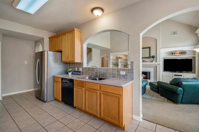 Standing between the breakfast nook and the kitchen, this view of the family room highlights the seamless flow between spaces. The kitchen features a double sink with an archway overhead and a counter-height bar that opens to the living room. To the left of the fridge, just out of sight, a doorway provides access back near the staircase, maintaining the home’s open and functional layout. | Image 12