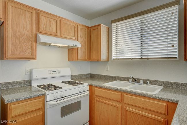 Kitchen with a sink, white gas range, light brown cabinets, light countertops, and under cabinet range hood | Image 10