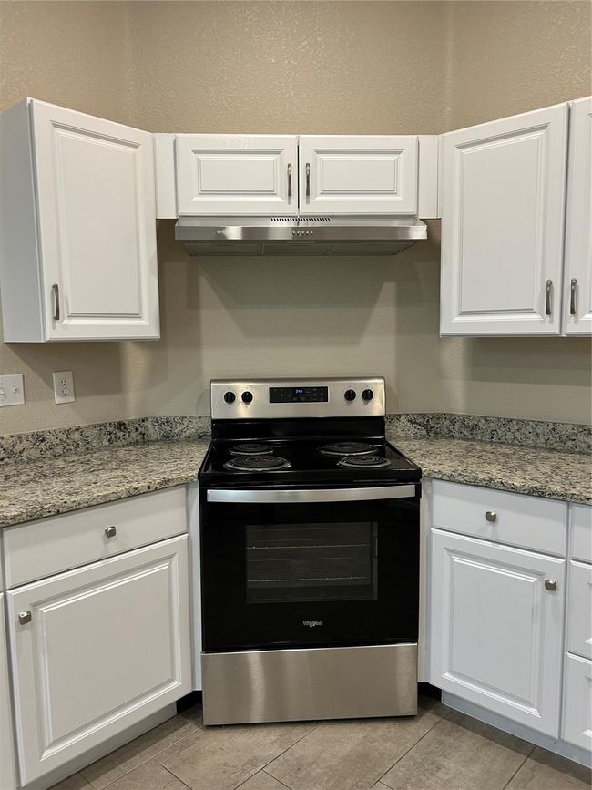 Kitchen with electric range, under cabinet range hood, white cabinetry, and light tile patterned flooring | Image 9