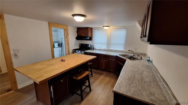 Kitchen with a sink, light wood-type flooring, wood counters, stainless steel appliances, and a breakfast bar area | Image 15