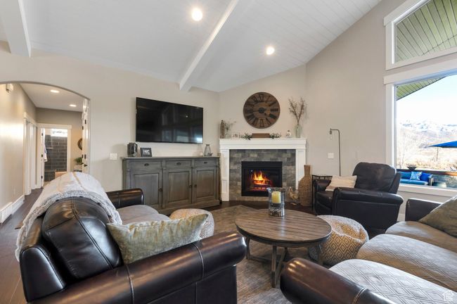 Living room with lofted ceiling with beams, arched walkways, a glass covered fireplace, recessed lighting, and dark wood-style floors | Image 9