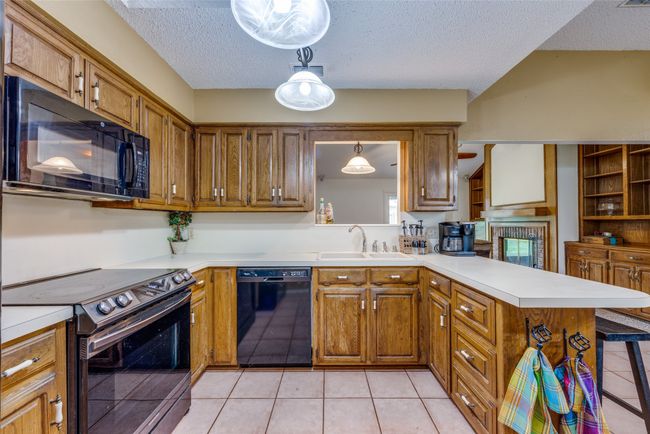 Kitchen with black appliances, a sink, a textured ceiling, brown cabinets, and light countertops | Image 6