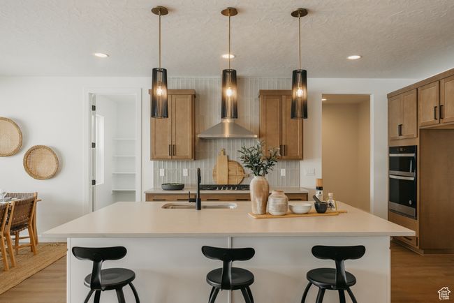 Kitchen featuring wall chimney range hood, a sink, light wood-style floors, decorative backsplash, and recessed lighting | Image 19