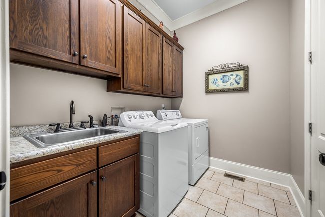 Plenty of storage space in this laundry room with lots of cabinetry and offers a sink, tile flooring, and extra storage. | Image 60
