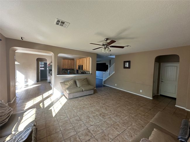 Unfurnished living room featuring arched walkways, ceiling fan, a textured ceiling, stairway, and light tile patterned floors | Image 4