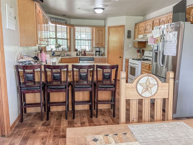 Kitchen with light brown cabinetry, stainless steel appliances, under cabinet range hood, light countertops, and a peninsula | Image 13