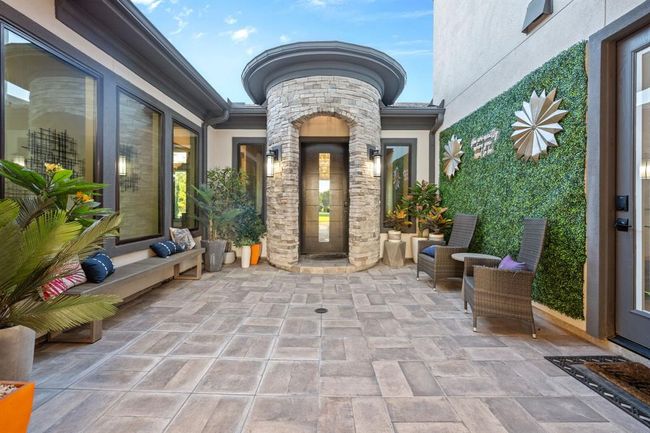 This inviting courtyard features a modern design with elegant stonework and large windows, complemented by lush greenery. Comfortable seating areas and stylish decor create a welcoming outdoor space, perfect for relaxation and entertaining. | Image 4