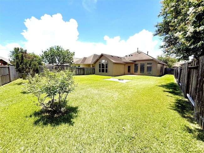 Spacious backyard with lush green lawn, mature trees, and a fenced perimeter. The house features large windows and a gabled roof, providing a bright and inviting exterior. Ideal for outdoor activities and privacy. | Image 28