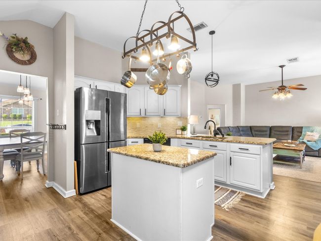 Kitchen with stainless steel refrigerator with ice dispenser, a peninsula, tasteful backsplash, white cabinetry, and high vaulted ceiling | Image 8