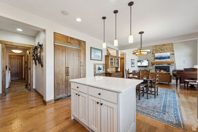 Kitchen featuring a fireplace, a center island, white cabinetry, decorative light fixtures, and light wood-type flooring | Image 13