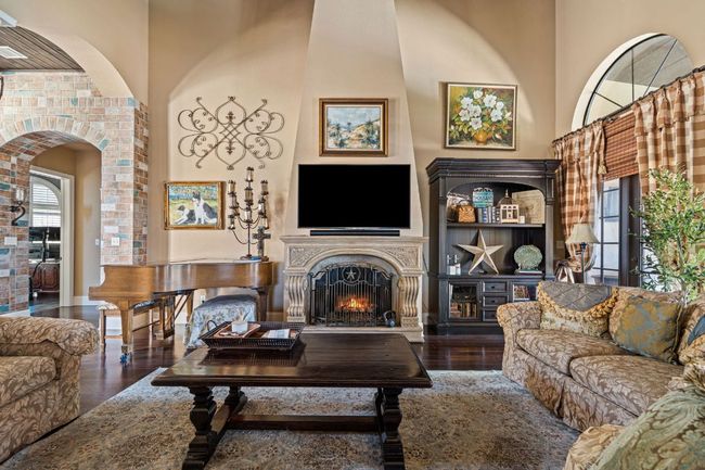Living area featuring arched walkways, wood finished floors, a high ceiling, and a warm lit fireplace | Image 9
