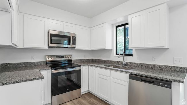 Kitchen featuring appliances with stainless steel finishes, wood finished floors, white cabinetry, and a sink | Image 7
