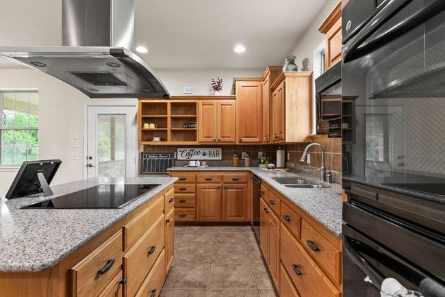 Kitchen featuring backsplash, open shelves, black appliances, island range hood, and a sink | Image 15