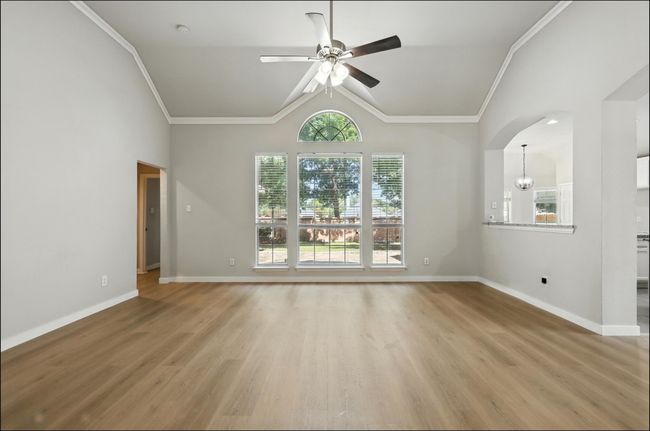 Empty room with a ceiling fan, light wood finished floors, lofted ceiling, and crown molding | Image 14