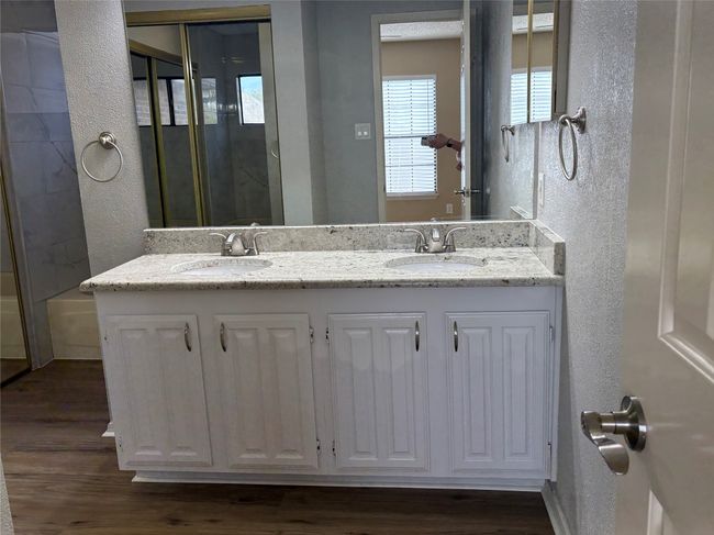 Bathroom with a textured wall, wood finished floors, double vanity, and a shower | Image 24