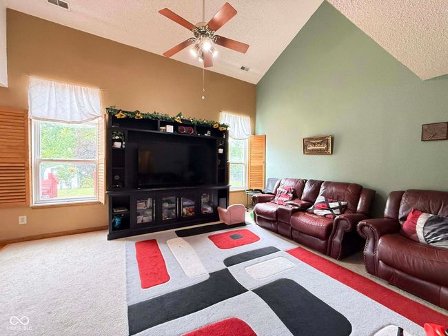 living area with a textured ceiling, a ceiling fan, carpet flooring, and high vaulted ceiling | Image 11