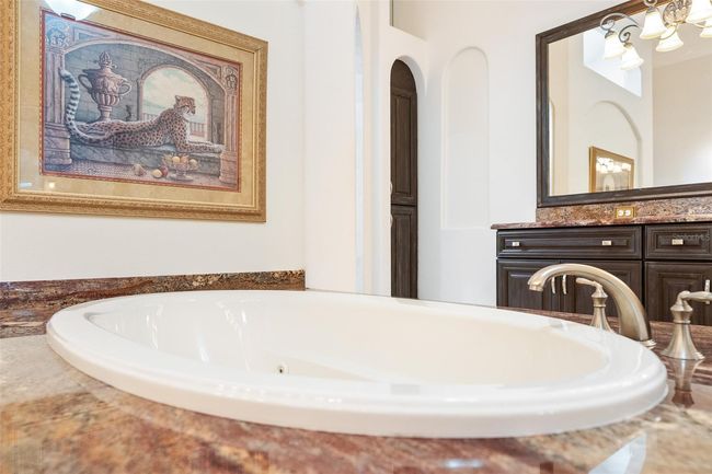 The spa-like soaking tub is beautifully framed by rich stone countertops, custom cabinetry, and elegant arches—offering a peaceful retreat for ultimate relaxation. | Image 11