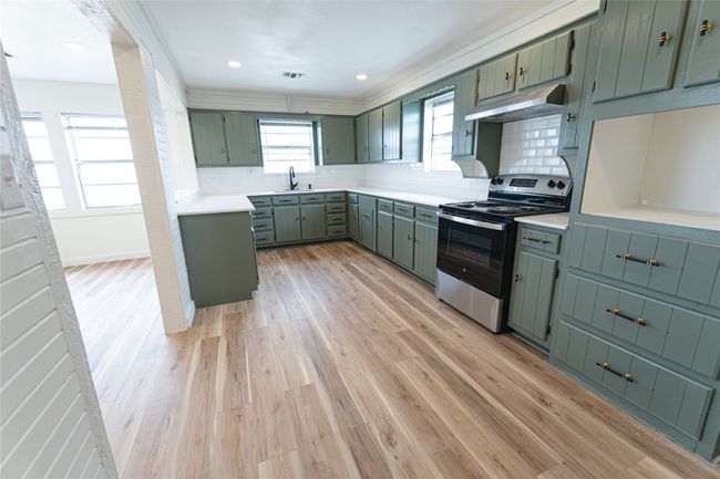 Kitchen featuring light wood-style flooring, electric stove, under cabinet range hood, a sink, and green cabinetry | Image 11