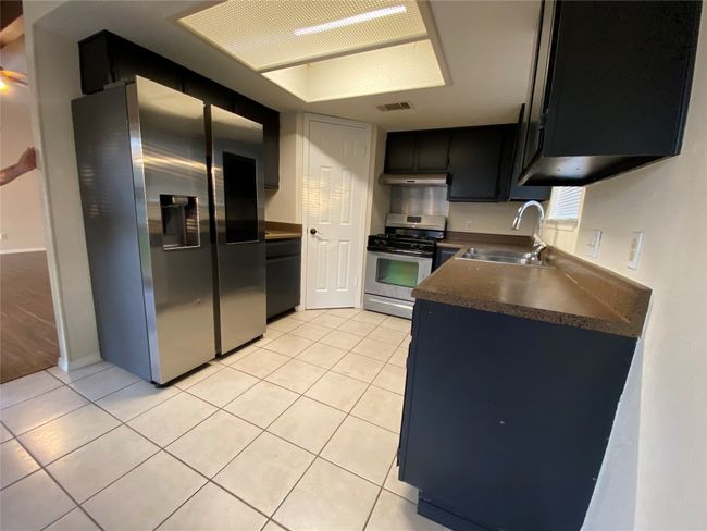 Kitchen featuring visible vents, under cabinet range hood, dark countertops, a sink, and stainless steel appliances | Image 14