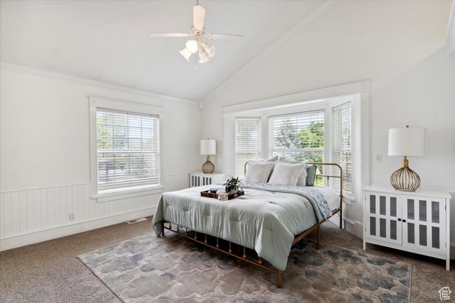 Bedroom with carpet floors, ceiling fan, high vaulted ceiling, and wainscoting | Image 16