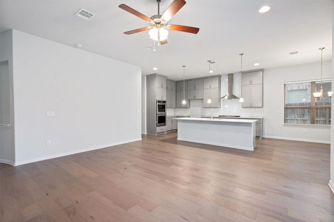 Kitchen featuring gray cabinets, wall chimney exhaust hood, tasteful backsplash, open floor plan, and visible vents | Image 9