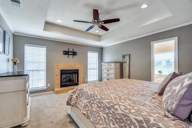 Carpeted bedroom with a raised ceiling, ornamental molding, a tile fireplace, recessed lighting, and ceiling fan | Image 24