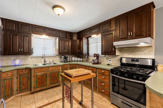 Kitchen with stainless steel range with gas stovetop, extractor fan, decorative backsplash, light tile patterned floors, and dark brown cabinetry | Image 5