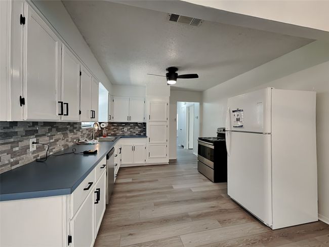 Kitchen with stainless steel appliances, dark countertops, white cabinets, and a ceiling fan | Image 5