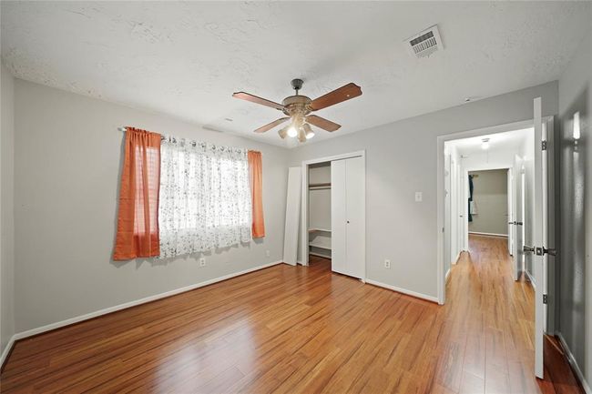 Bedroom located on the opposite side of the house from primary bedroom, features wood vinyl plank flooring, a ceiling fan and a closet with sliding doors. The space opens to a hallway with another bedroom visible. | Image 21