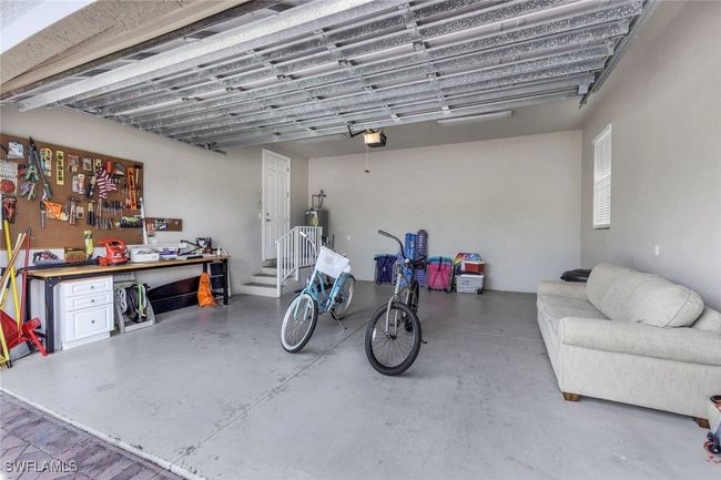Garage featuring a garage door opener, electric water heater, and a workshop area | Image 25